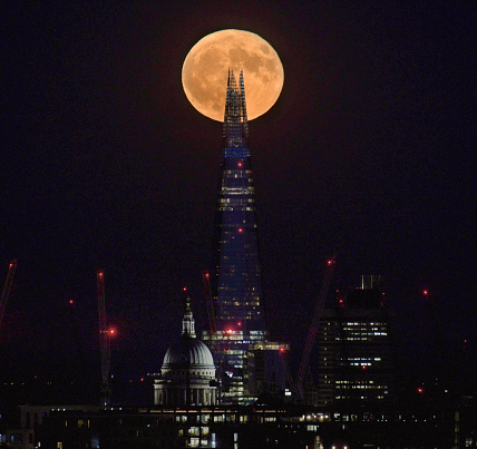 The full moon rises over the City of London skyline, UK