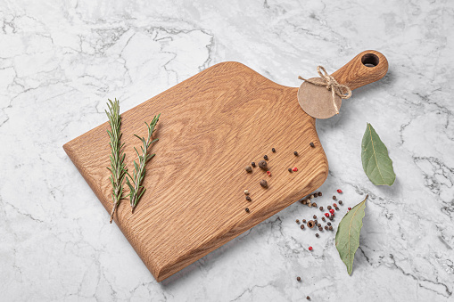 square wooden cutting board with a handle. thyme and spices on a white marble background. mockup with copy space for text, side view