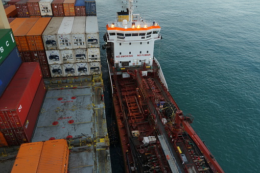 Barcelona, Spain - 06 09 2022: Aerial view on bunker barge with red hull and white superstructure alongside of the loaded container vessel during transferring of fuel or bunkering. Ship is moored.