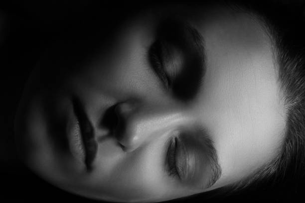 Portrait of a young woman who has pulled the collar of her sweater halfway over her face with both hands. Her eyes are closed. The mood is depressed.