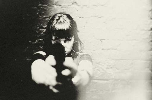 Portrait of a young woman with a pistol. She looks directly, focused and sternly at her opposite. She is ready for anything. Dark and mysterious, Film Noir style.