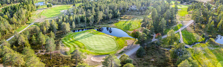 Aerial panorama view on golf course in Northern forest. Unidentified people play walk to change Golf course, pine trees around. Warm Sunny day excellent for golfers. Umea, Sweden - September 21, 2020