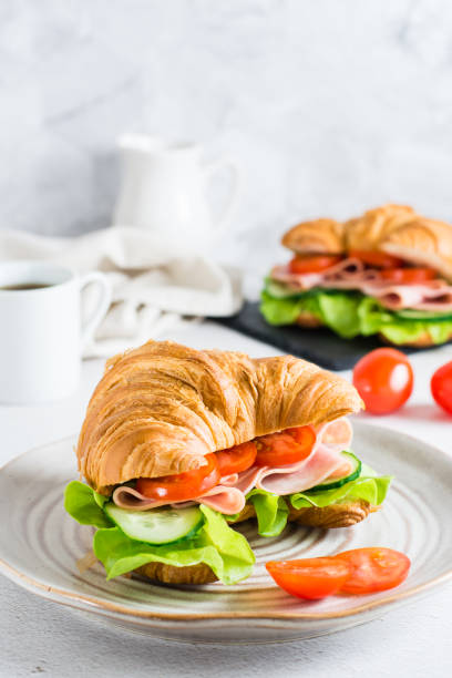 istock Fresh croissant sandwich with ham, vegetables and lettuce on a plate. Vertical view. 1403889526