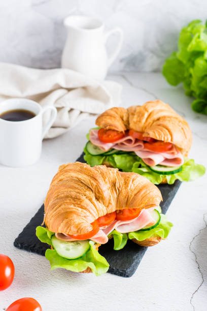 istock Croissant sandwiches with ham, lettuce and vegetables on a slate on the table. Vertical view 1403889556