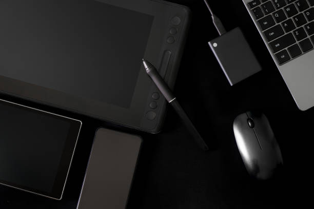 istock Stylus and graphics tablet with screen on a black background next to laptop, computer mouse, external ssd drive and mobile gadgets. Concept of modern creativity and digital devices 1403890135