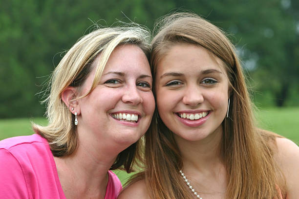 Mother and daughter outdoors in a meadow spending time together.Mother looking and camera and little girl hugging her