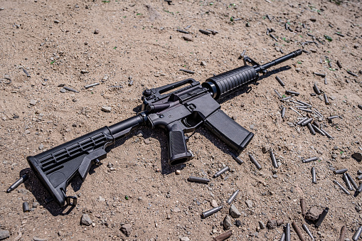 An assault/carbine style rifle with .223 and 5.56 casings around it in the dirt.