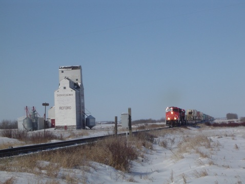 A train passing an abandoned grain elevator on a prairie winter day.