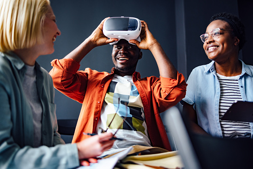Excited African-American student takes off virtual reality simulator and laughing with his multi ethnic group of friends.