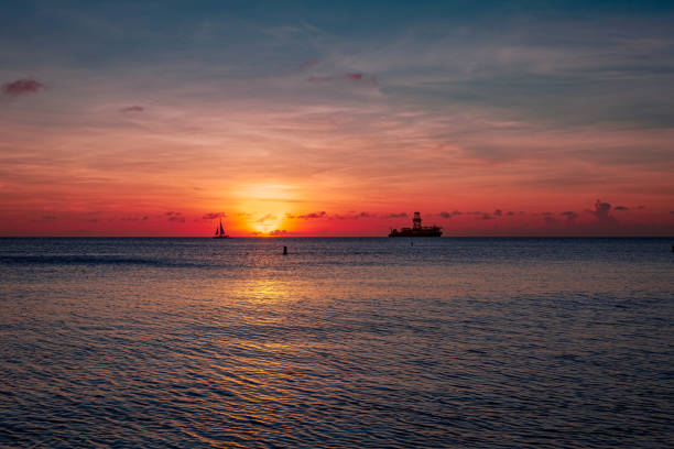 tramonto al largo della costa occidentale di aruba nel mar dei caraibi. silhouette della barca all'orizzonte e nave da esplorazione petrolifera - sailing sailboat sunset aruba foto e immagini stock
