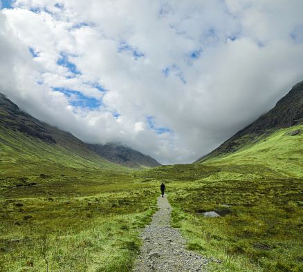 Hiker on a trail through the dramatic valley landscape near Bauchaille Etive Beag in Glencoe of the Scottish Highlands