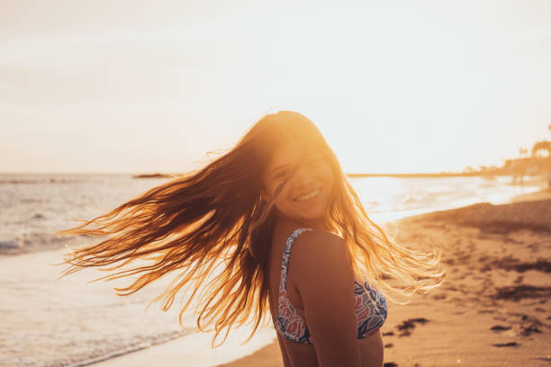 una giovane donna caucasica che guarda la macchina fotografica sorridendo e divertendosi in spiaggia. adolescente persona femminile che si gode il tramonto all'aperto. - only teenage girls teenager adolescence sea foto e immagini stock