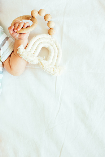 Baby playing with a wooden toy on white linens background. Mockup. Top view. Copy space.