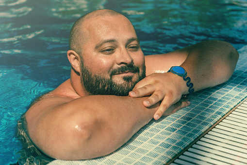 Portrait of plus size big happy smiling man relaxing in swimming pool.