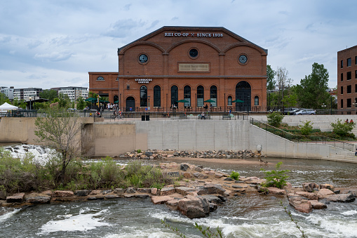 Denver, Colorado, May 28, 2022. Front View of the REI historical building, and Starbucks along the South Platter River Trail, from across the river