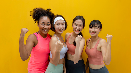 Group portrait of healthy and slim diversity athlete women in sportswear smiling on the isolated yellow background for exercise and workout concept
