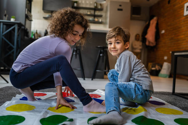 Brother and sister siblings small caucasian boy and girl child play twister game on the floor at home alone real people family growing up leisure concept copy space