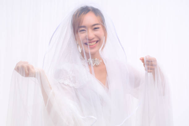 studio portrait of happy asian bride in white gown with veil posing on white background