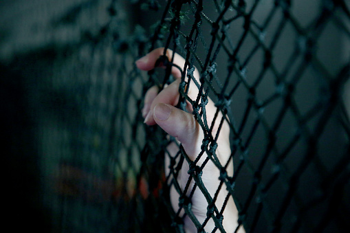 Human hand is holding on wire mesh fence.