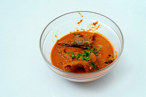 Chicken curry or masala , spicy reddish chicken leg piece dish garnished with coriander leaf ,which is traditionally arranged in a brass bowl  with white background