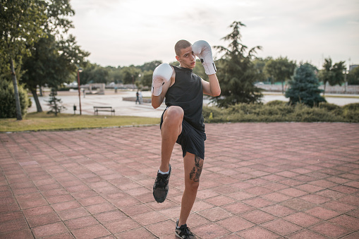 A young kickboxer with boxing gloves trains in the park, outdoors
