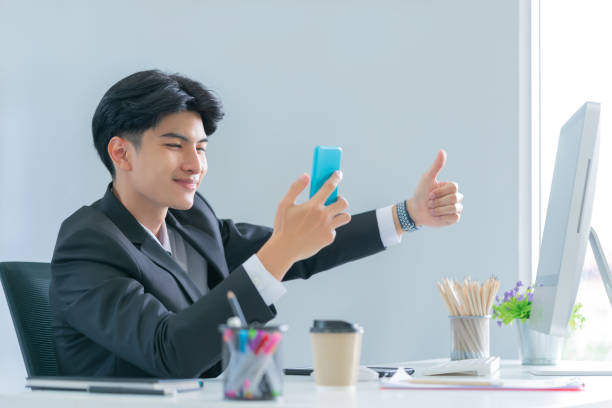 istock Business man showing ok thumb up gesture while talking on mobile phone in the office. 1403931556