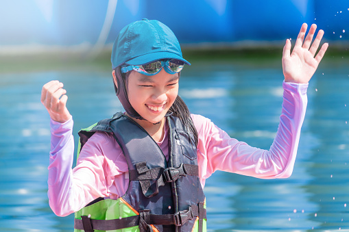 Asian girl is smiling while having fun in a water park with full swim suit and safety on.