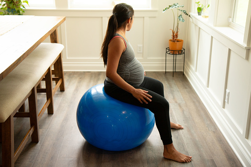 Young latina in her 9th month of pregnancy doing pelvic exercises on fitness ball.