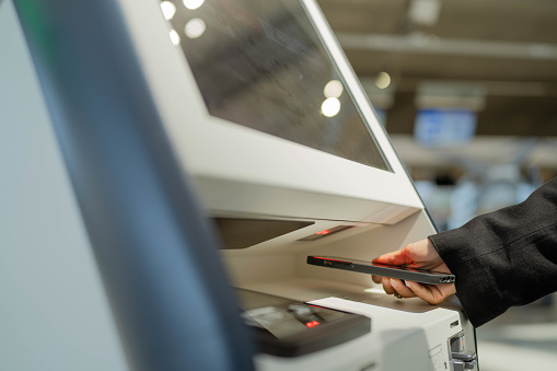 Two Asian business woman holding passport and  using self check-in kiosk in airport terminal to travel to work.