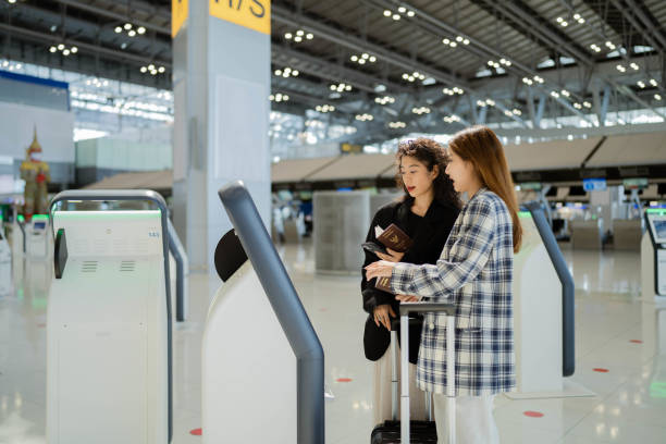 two young asian business woman doing self check in at the airport. - self service stockfoto's en -beelden