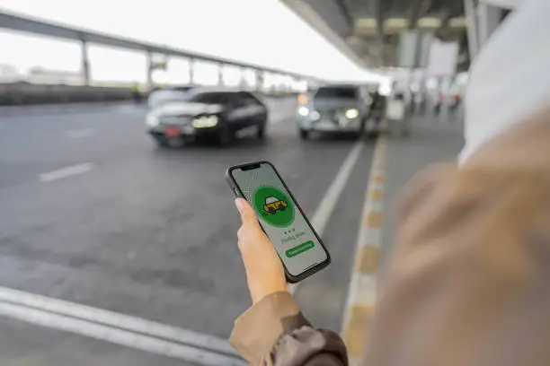 Young muslim woman using mobile app device to order a taxi pick up service by the urban road at airport.