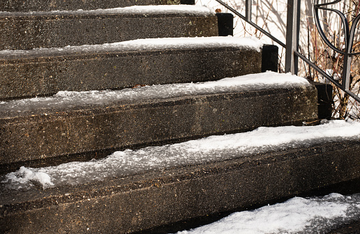 side view to stone steps of an outdoor stairway with melting snow on a sunny day in winter