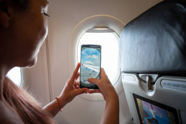 une jeune femme prenant une photo depuis la fenêtre d’un avion - airplane smart phone travel mobile phone photos et images de collection