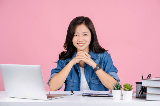 美しい若いアジア人女性が微笑み、白いオフィスデスクに座って仕事をしています。達成キャリアコンセプト。 - looking at camera smiling desk isolated ストックフォトと画像