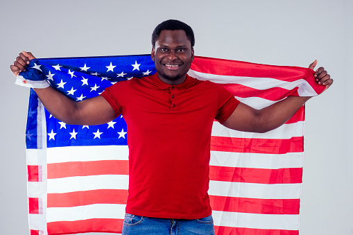 african american man looking at camera and proudly holding american flag at studio