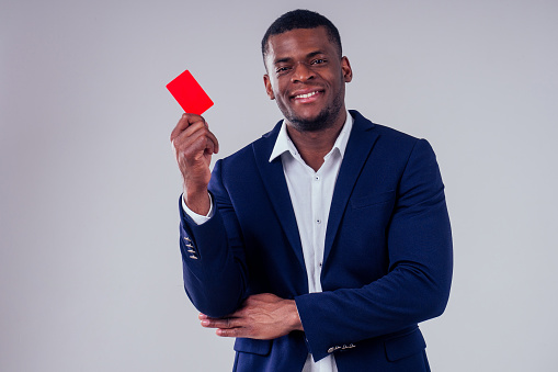stylish african american in costume black pants and jacket with a big shirt collar holding red credit plastic card in studio on white background, badge my name is
