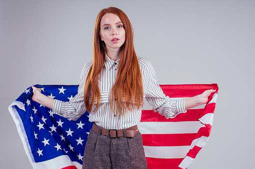 happy young and beautiful redheaded businesswoman holding American flag on white background in studio : independence day usa 4th of july,English language learning