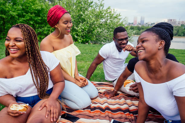 happy casual america african people having fun and eating burger outdoors lifestyle,students for a break summer evening cloudy weather in park stock photo