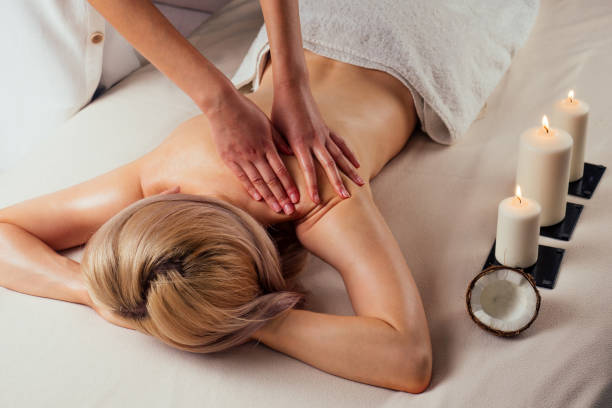 ayurvedische entspannung.gesundheit schönheit glückliche blonde frau im spa-salon bekommt massage. schönes mädchen, das day spa resort genießt und sich auf den tisch neben dem kerzenfeuer legt - ayurveda women spa treatment health spa stock-fotos und bilder