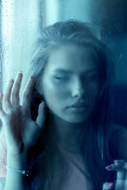 Sad young woman looking through window on rainy day