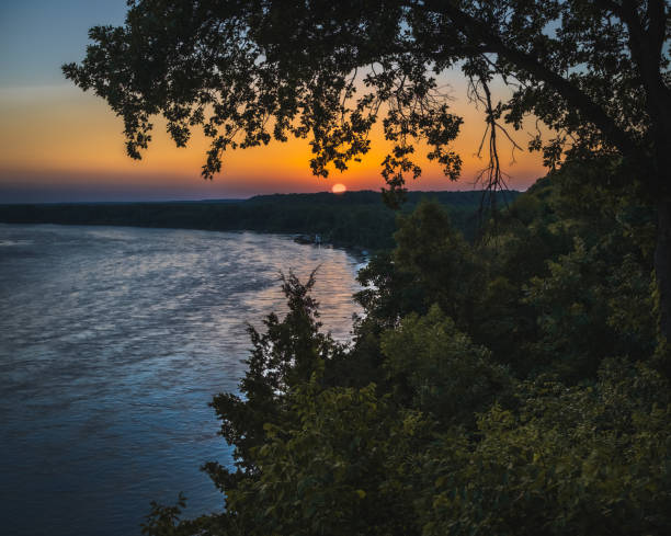 Sunset on Missouri River on nice summer evening; trees on foreground; setting sun in background