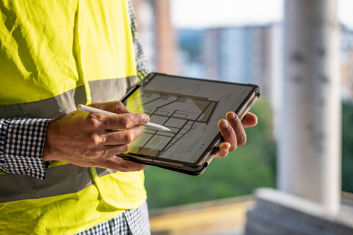 Engineer comparing the projects on his tablet with the actual work done on the site. Man working in the construction industry.