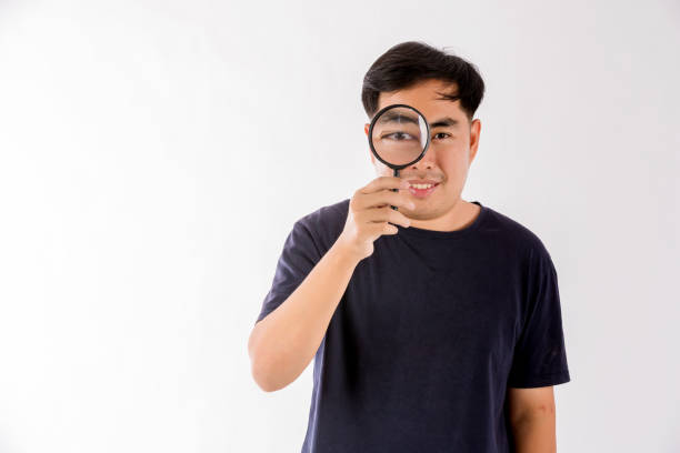 istock Man holding magnifying glass on white background. man with a magnifying glass in studio. Positive curious man in casual wear looking at through magnifier 1403949444