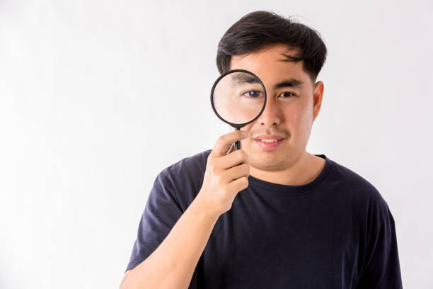 istock Man holding magnifying glass on white background. man with a magnifying glass in studio. Positive curious man in casual wear looking at through magnifier 1403949446