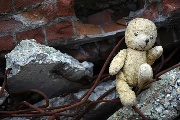 A old used teddybear between rubble. Can be used depicting effects of war and bombing.