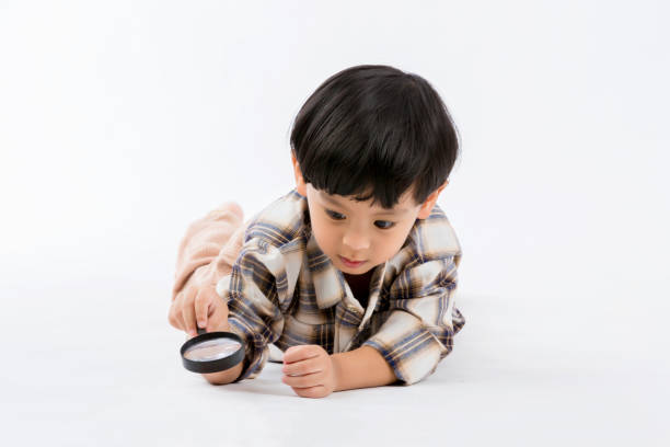 istock Child holding magnifying glass on white background. Boy with a magnifying glass in studio. 1403949605