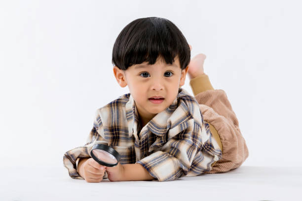 istock Child holding magnifying glass on white background. Boy with a magnifying glass in studio. 1403950457