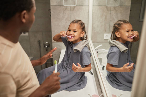 Happy Girl Brushing Teeth with Father High angle portrait of cute black girl brushing teeth with dad in bathroom and smiling happily teeth bonding stock pictures, royalty-free photos & images