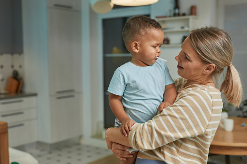 Portrait of happy Caucasian mother holding cute toddler boy in home kitchen interior, copy space