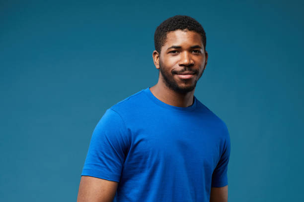 Handsome Black Man on Blue Portrait of smiling black man wearing blue shirt on vibrant blue background and looking at camera, copy space blue t shirt stock pictures, royalty-free photos & images